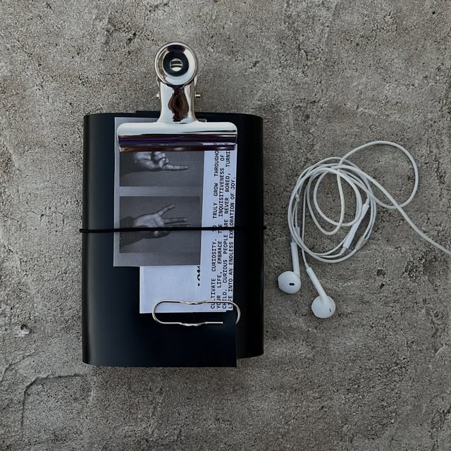 Black leather journal with a monochrome collage and silver clips beside a pair of earphones